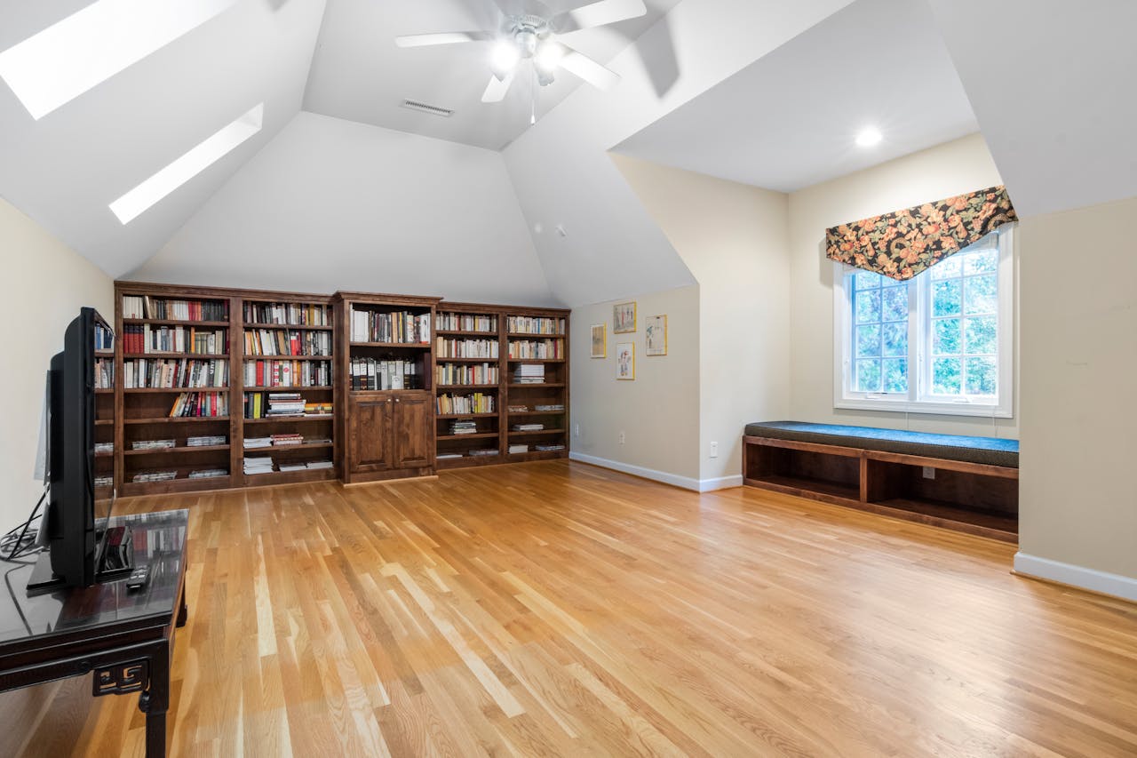 services-03 Bright attic room with wooden floors, large bookcase, and natural light through skylights.